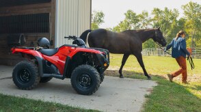 Rancher stationary in front of barn. Woman leading horse out fo the barn in background.
