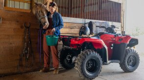 Woman at rear of ranger in barn. Horse in pen in background.