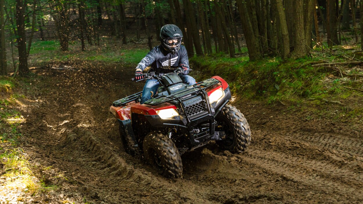 Driver on Rancher going left on a very muddy trail. Wood landscape in background.