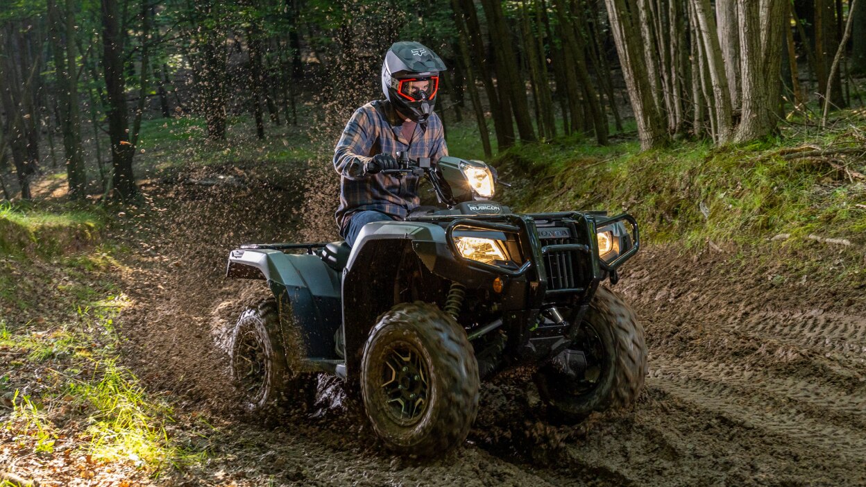 Rider on Rubicon going right on dirt track in woods. Wet dirt around ATV.