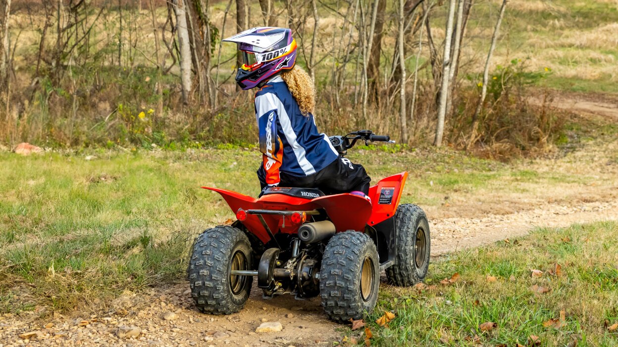 Rear view of young rider on ATV in Field.