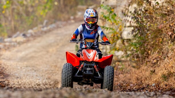 Young rider on ATV on dirt road. Front facing.