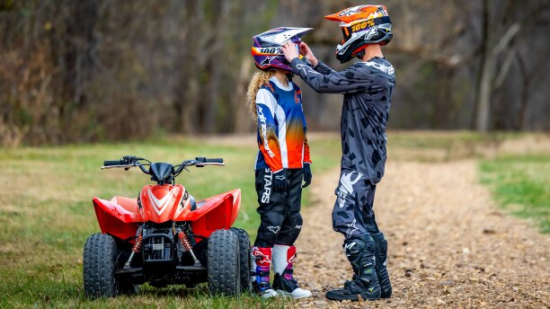 Young rider with Adult rider holding their helmet. Beside ATV.
