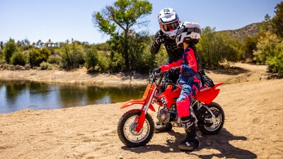 Young rider on bike with instructor on dirt track. Lake in background.