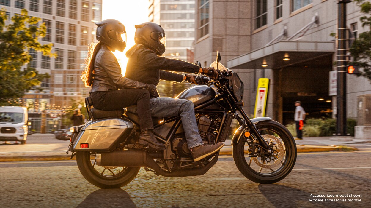 Rider and passenger on road in city. Sunset in background. Accessorized model shown.