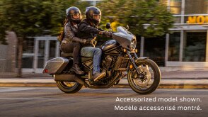 Rider and passenger going right on Rebel 1100 Touring on road. Building, side walk and trees in background. Accessorized model shown.