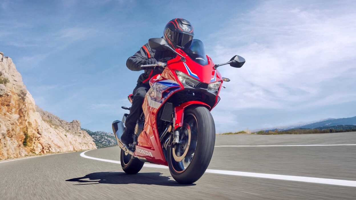 A small image of a person riding a red sport motorcycle near the coast.