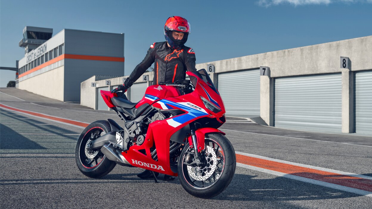 A small image of a person riding a red sport motorcycle along a coastal road.