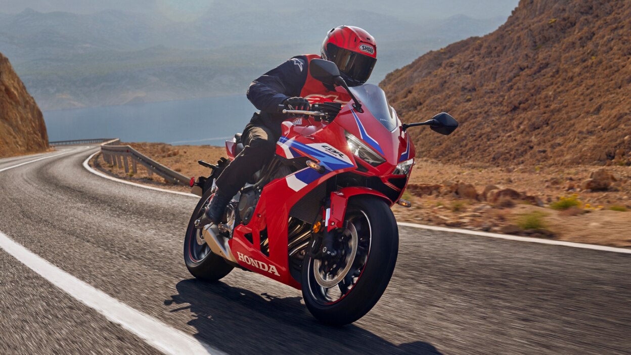 Rider making right turn on road. Mountain and rocky landscape in background.