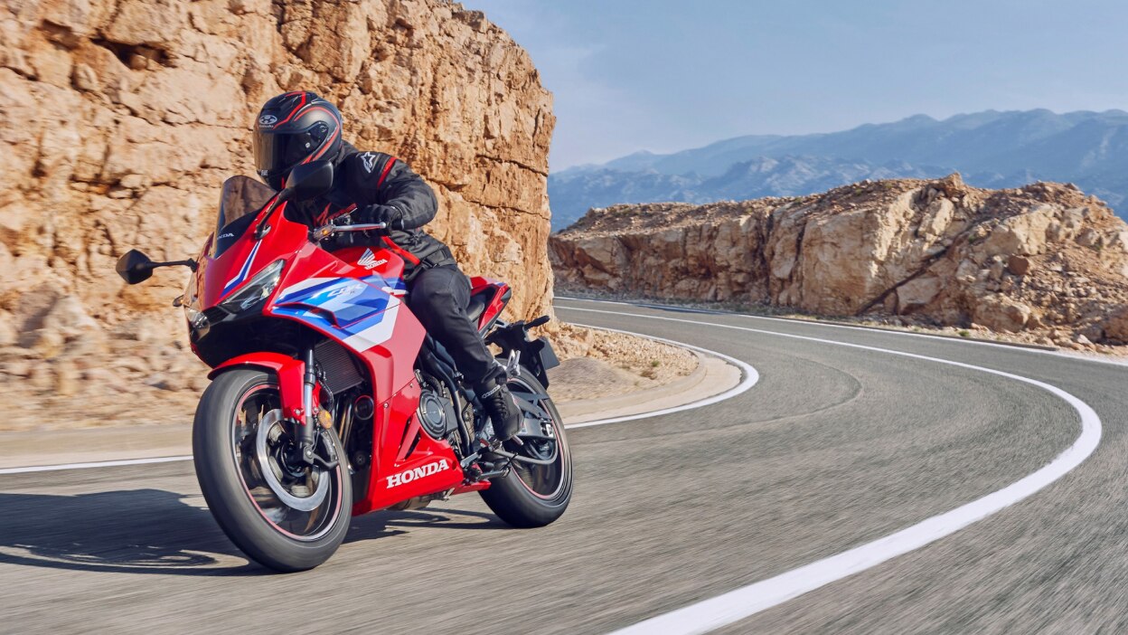 Rider making right turn on road. Mountain and rocky landscape in background.