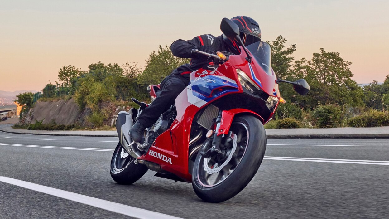 Rider making right turn on road. Bushes and tress in background.