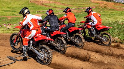Rear view of lineup of riders on motorcycles on dirt track.