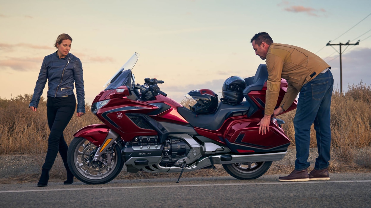 Left side image of Gold Wing Tour Airbag, stationary on road. A woman is walking at the front of the bike and a man is at the rear.