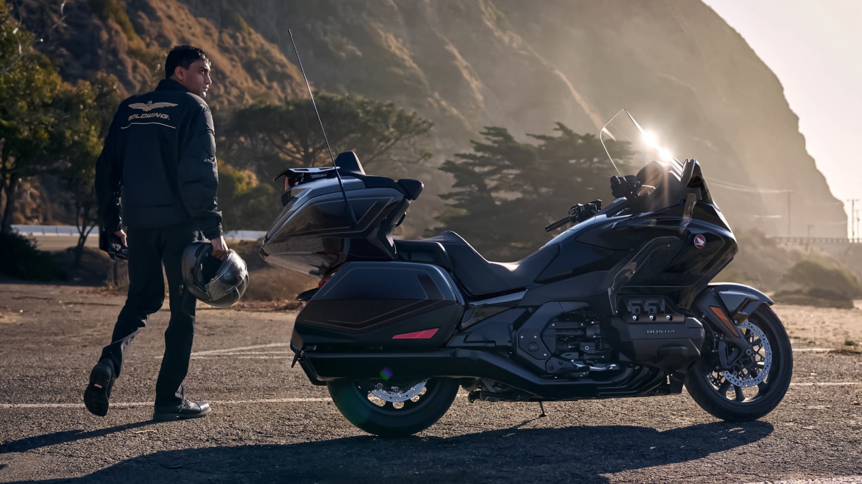 Right image of Gold Wing Tour stationary on road. Rider with helmet in hand standing to the right of Gold Wing Tour.