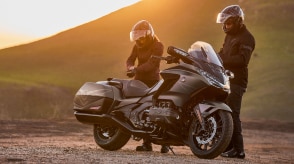 Gold Wing stationary on road, left facing. Two riders with helmets on behind Gold Wing.