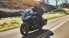 Two people riding a touring motorcycle on a winding road.